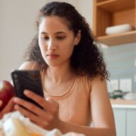 A woman uses a carb tracker on her phone as she holds an apple to help understand how carbohydrates and diabetes are connected.