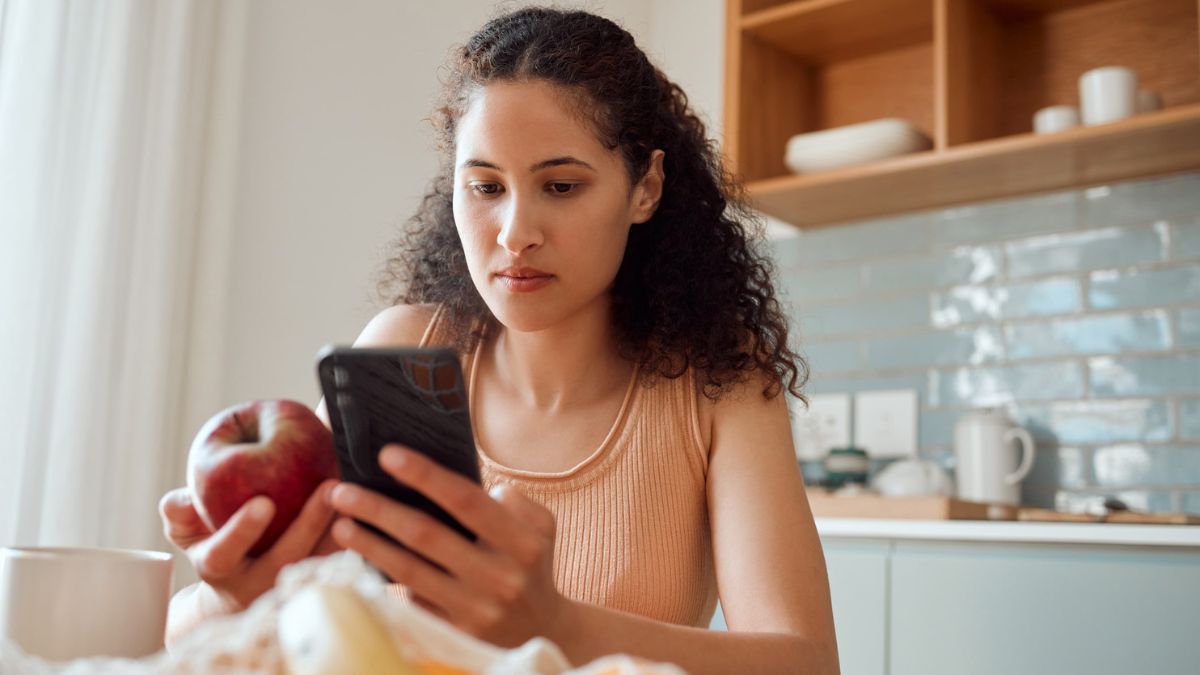 A woman uses a carb tracker on her phone as she holds an apple to help understand how carbohydrates and diabetes are connected.