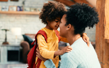 Affectionate African mother talking to her small daughter while saying goodbye before going to school for the first time.